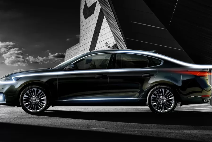 Black sedan with illuminated trim driving past a modern building with a large number 7 design.